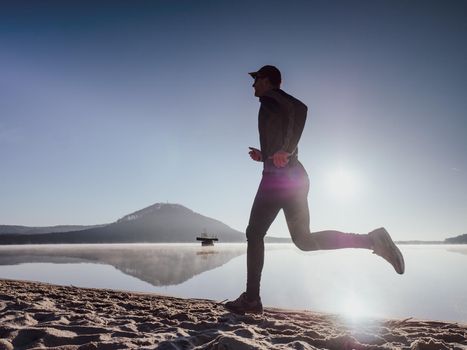 Full length of healthy man running and sprinting outdoors. Male runner. Man running on the beach at sunset.