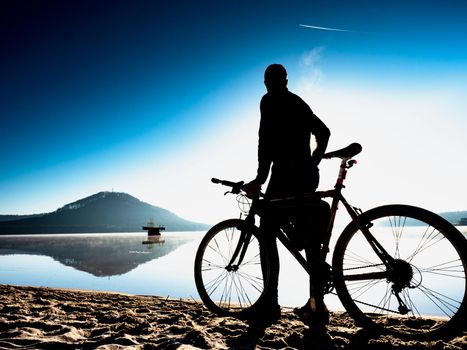 Man biker sit on bike frame and watch the calm lake within sunrise.