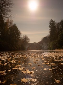 Frosty night with full moon light. Frozen lake with colorful leaves, round Rakotzbruecke, the Devil's bridge,  in light morning mist.  Kromlau park, Germany