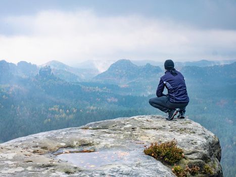 Man sitting at the peak of a mountain on a foggy morning.  Sit squatting on the peak edge and enjoying mountains view valley during heavy mist