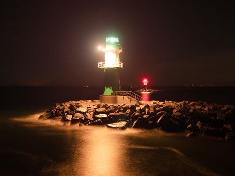 Westmole Leuchturm, shining signal light of breakwater at the mouth of a harbor.  November night, Warnemuende Strand, Germany