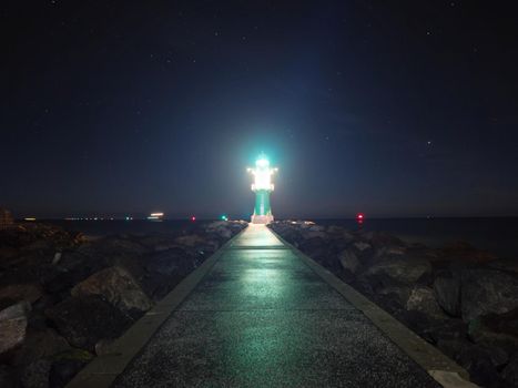 Westmole Leuchturm, shining signal light of breakwater at the mouth of a harbor.  November night, Warnemuende Strand, Germany