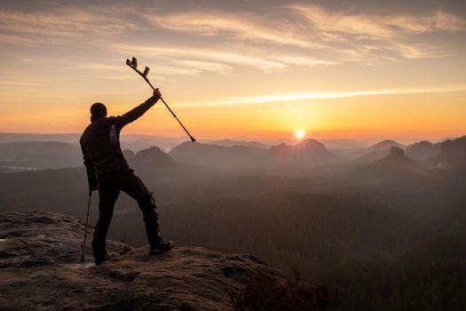 Silhouette of happy man with arms outstretched holding crutches standing by mountain valley  during sunset. Personal motivation