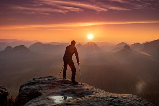 Disabled tourist with crutches. Rear view of Hurt hiker man with forearm poles walking against mountain sunset background 