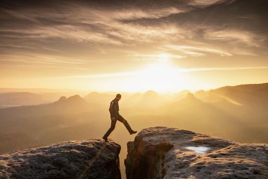 Strong mountain climber hiking and jumping over  the summit ridge of a peaks at sunset. Man takes leap of faith off of rock outcropping