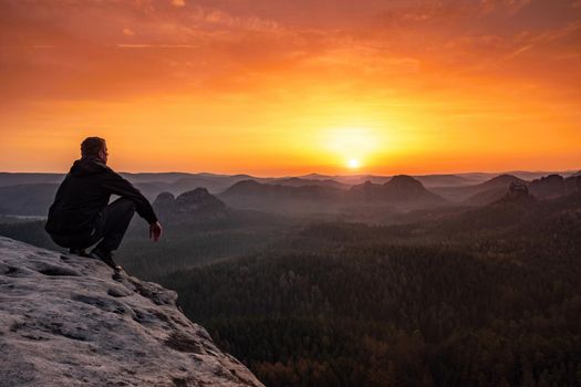 Mature man sit  on top of mountain, daybreak moment. Squating hiker 