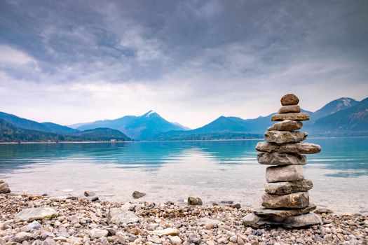 Pile stones on the beach. Rock heap of gray dolomite pebbles close to blue alpine lake, mountains silhouettes in bakground. 