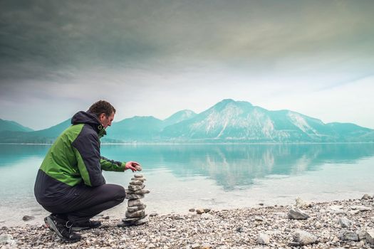 Cairn building. Hiker builds rock cairn from sharp dolomit stones at Alpine lake. Spring in European Alps.