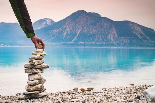 Cairn building. Hiker builds rock cairn from sharp dolomit stones at Alpine lake. Spring in European Alps.