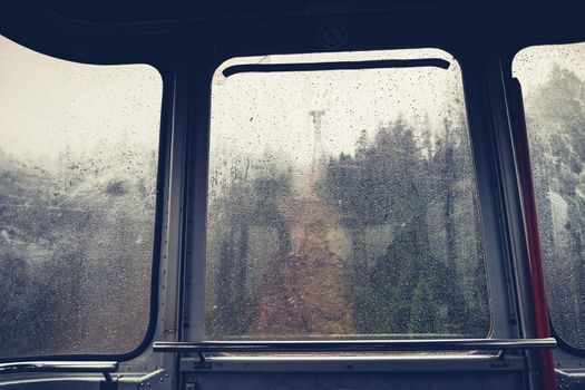 Raindrops on glass window of cableway. Sad view from overhead cable Car. Rainy weather during trip in mountains