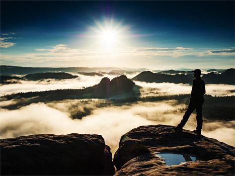 Man standing on a rock sorrounded by clouds on trek summit. Winterberg rock in the Saxon Switzerland National Park and photographs the sunrise.