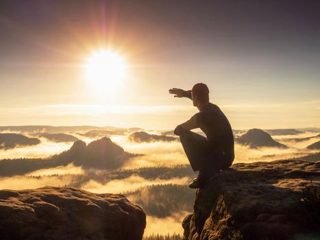 Man hiker squatting and shadowing eyes.  Hiker enjoy amazing view into mountain valley and enjoy adventure.