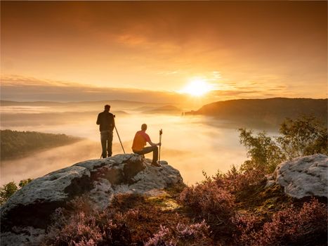 Two matured  photographers at the hilltop with his tripod and camera search of good object to make a final photography session at sunset time.