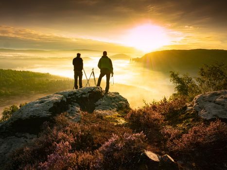 Two landscape photographers taking photos of mountain range during sunrise and heavy mist  in beautiful nature view  