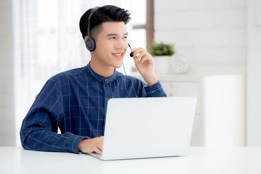 Young asian businessman working on laptop computer wearing headphone at home, business man wearing headset for video conference, communication and education, male study and learning for e-learning.