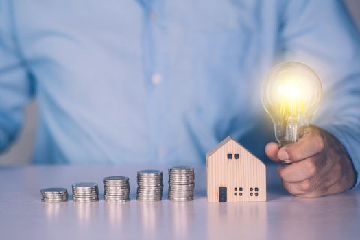 Hands of businessman hold light bulb and stack of coin with saving money for real estate and success, finance and investment, insurance home and deposit, residential and financial, business concept.