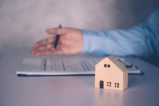 Real estate agent holding home and signing contract about agreement of real property on desk, house broker and planning investment, businessman writing on document form rent house, business concept.