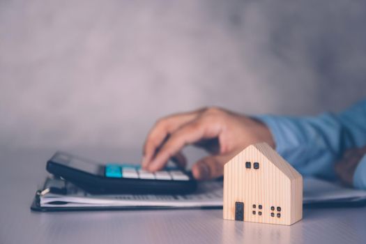 Businessman calculate with calculator about investment and having document on clipboard and home model on desk, insurance and finance, planning about real estate and residential, business concept.