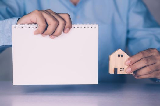 Hands of businessman holding home model and blank notebook, finance and residential, loan and mortgage of real estate, property and residence, investment with financial, business concept.
