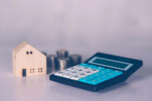 Investment about home with calculator and model house and coins on desk, property and real estate and mortgage, loan and finance, financial saving and account for residential, business concept.