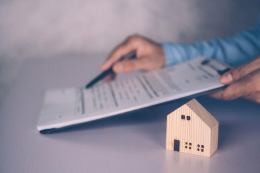 Real estate agent holding home and signing contract about agreement of real property on desk, house broker and planning investment, businessman writing on document form rent house, business concept.