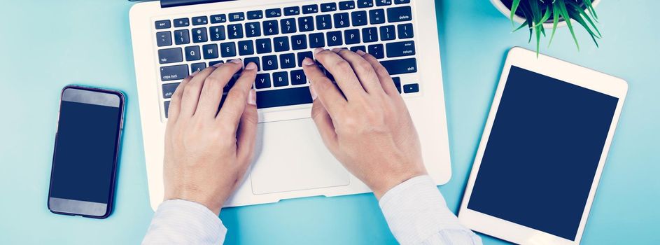 Hand of businessman working on laptop computer with plant and tablet and phone on desk in office, hand typing keyboard on notebook and workplace with copy space, top view, flat lay, business concept.