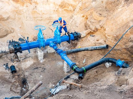 Man test valve in trench in ground with  large water pipeline of potable water delivery company