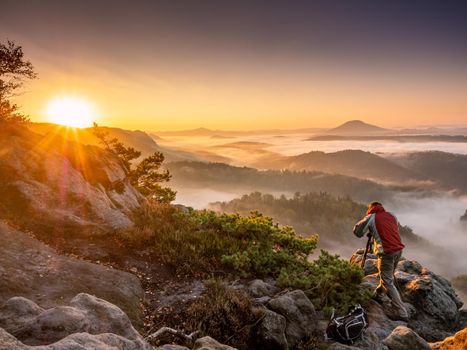 Man photographing in high mountains. Photographer hiking talking photos using SLR camera in fall autumn forest