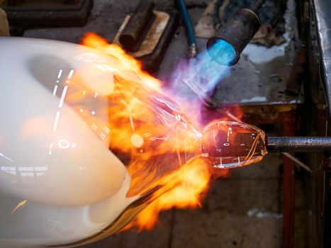 Master glassmaker heats a fire torch glass ball on a glass pipe. Hand shaping hot glass in a glass design studio in Kunratice.