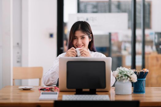 Charming asian businesswoman looking at camera and working with laptop computer in office.