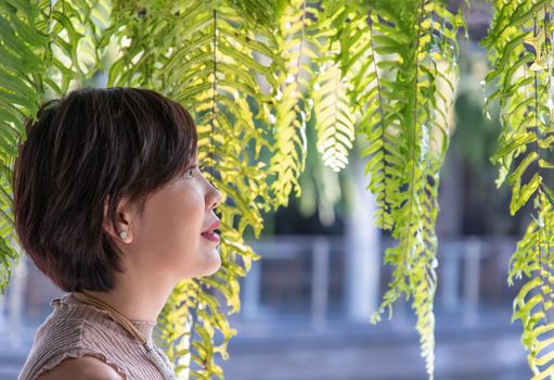 Portrait of a young Asian woman enjoy and relax on green ferns leaves background. Side view, Happy woman in nature concept, Selective focus.