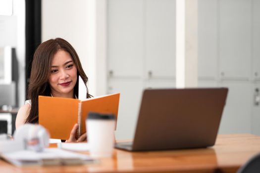 Attractive asian woman working with laptop computer during reading lecture on notebook at home.