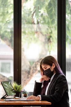 Vertical shot of asian businesswoman wearing face mask while working with financial calculator on a computer in the office.