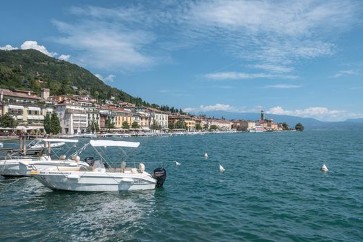 Salò (BS), ITALY - August 25, 2020. Panoramic view of the historic part of Salò on Lake Garda Italy. Tourist site on Lake Garda. Lake in the mountains of Italy. White boats are docked.