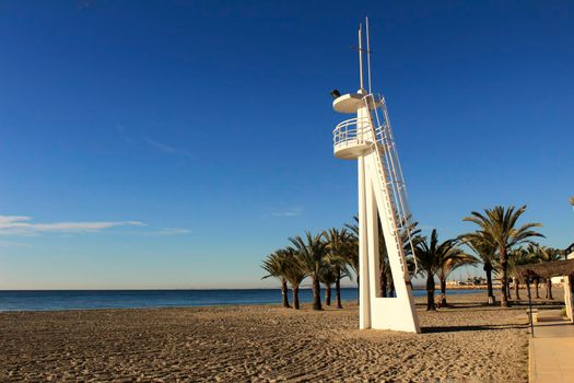 Lifeguard tower on a quiet and lonely beach in a sunny day in southern Spain, Alicante. Palm trees in the background.