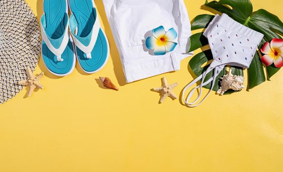 Summer and vacation concept. summer accessories with clothes, shoes, tropical leaves and flowers, flat lay on yellow background
