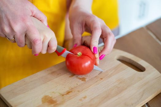 Cropped image of Young Mother Helping Daughter to cut tomato with kitchen knife on cutting board, teaching child to cook