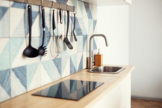 Kitchen spatulas handing on railing on a tiled wall with a blue geometric pattern in the modern designed kitchen room in a Scandinavian stayle. Kitchenware object and interior photo.