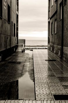 Lonely Little street between buildings facing the sea after a rainy day. Black and white Photography