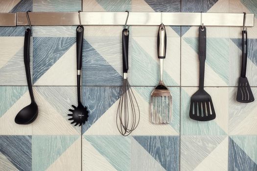 Kitchen spatulas handing on railing on a tiled wall with a blue geometric pattern in the modern designed kitchen room in a Scandinavian stayle. Kitchenware object and interior photo.