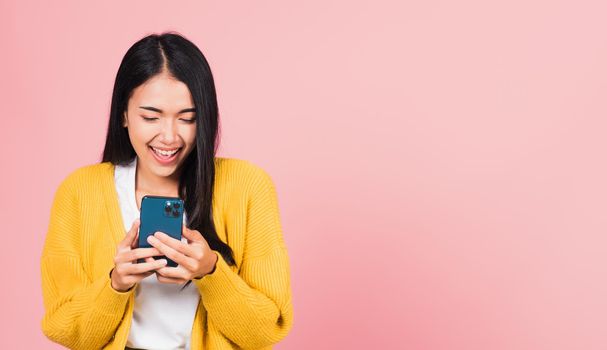 Happy Asian portrait beautiful cute young woman teen smiling excited using smart mobile phone studio shot isolated on pink background, Thai female surprised making winner gesture on smartphone