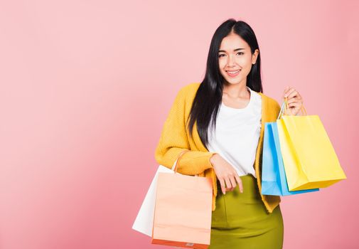 Portrait of Asian happy beautiful young woman teen shopper smiling standing excited holding online shopping bags colorful multicolor in summer, studio shot isolated on pink background with copy space