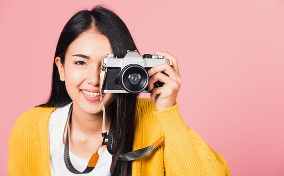 
Attractive energetic happy Asian portrait beautiful young woman smiling photographer taking a picture and looking viewfinder on retro vintage photo camera ready to shoot isolated on pink background