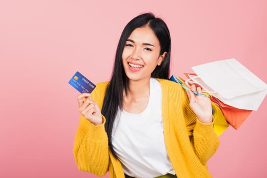 Portrait Asian happy beautiful young woman shopper smiling standing excited holding online shopping bags colorful and credit card for payment on hand in summer, studio shot isolated on pink background