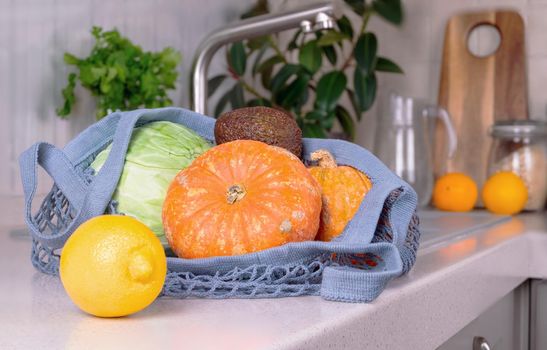 An eco-friendly shopping bag with vegetables lies on the work surface in the eco-friendly kitchen. Environmental protection concept, zero waste, recyclable. Selective focus.