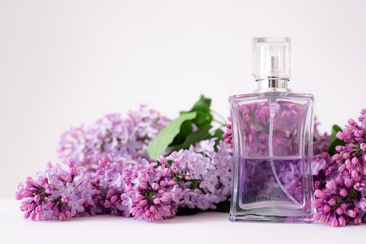 A bottle of perfume and lilac on a white background . Women's perfume. Spring fragrance. Aromatherapy. Nice smell. Beauty and fashion. Article about the choice of fragrance. An article about current flavors . copy space. A branch of lilac. Nature