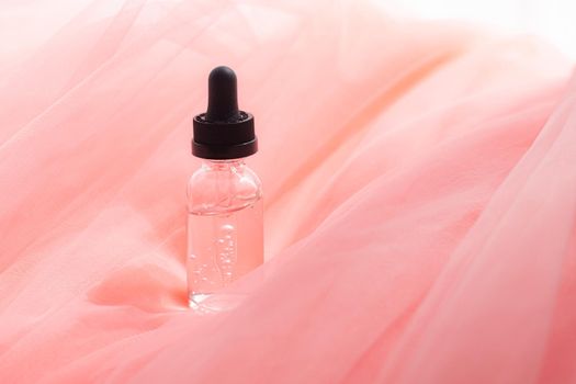Hyaluronic acid bottle on coral fabric . Beauty container. Skin care. Vitamins for the skin. Rejuvenation. Female beauty. An article about the benefits of hyaluronic acid. Article about the choice of hyaluronate. Copy space.