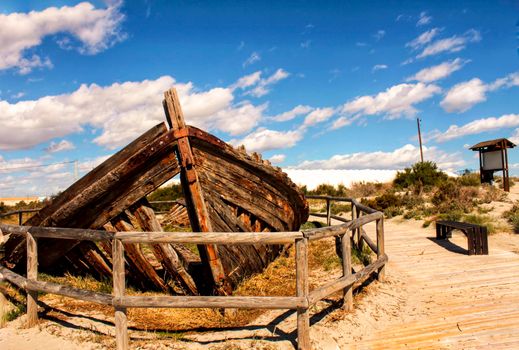 Old abandoned boat on the beach in Santa Pola. Salinas in the background under blue sky
