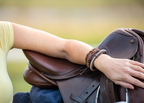 Woman leaning casually one arm on saddle in a rural country location.