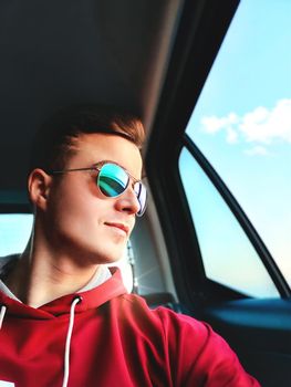 A young smiled man is sitting in the back seat of a taxi cab going to the airport and taking selfie